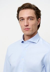 Lichtblauw overhemd met lange mouwen, gemaakt van gladde stof, voorzien van een puntige kraag, knoopsluiting aan de voorkant en subtiele stikdetails.