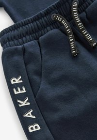 Pantalones de chándal azul marino hechos de tela suave con una cintura elástica, con texto blanco "BAKER" en el lateral y cordones negros.