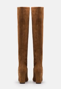 Brune ruskindsstøvler, der rækker over knæet, med en glat tekstur, firkantede høje hæle og enkel sømdetalje på bagsiden.