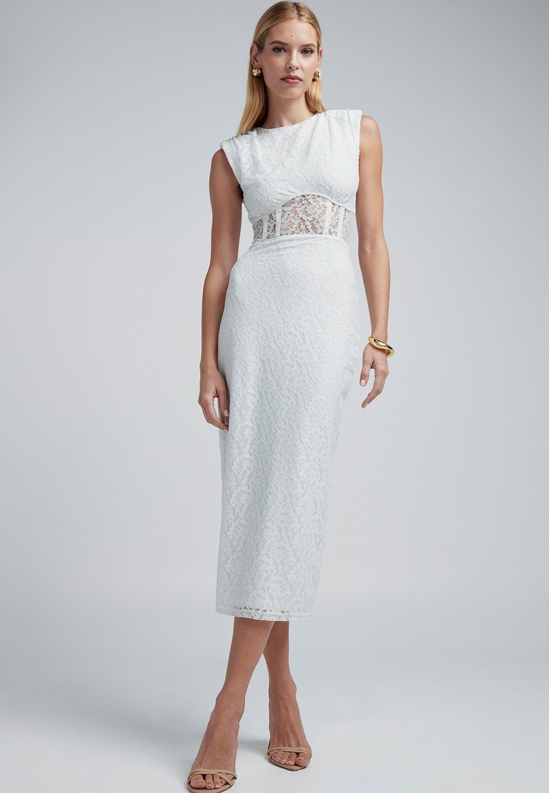 Robe en dentelle blanche à silhouette ajustée, manches courtes, avec un panneau en dentelle transparente à la taille, présentant une texture lisse et un ourlet à la cheville.