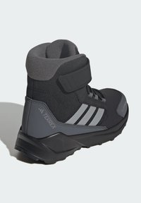 Black and gray mid-cut boot with a Velcro strap, textured upper, three white stripes, and a rugged sole for traction.