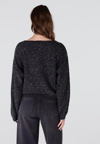 Zwarte trui met een comfortabele pasvorm, voorzien van een gestructureerd oppervlak en verspreid over de stof glinsterende pailletten. Ribbelboord onderaan en lange mouwen met een lichte ballonvorm.
