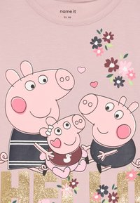 Gaiši rozā T-krekls ar multfilmu cūku ģimenes dizainu. Iezīmē ziedu akcentus un spīdīgu "HELLO" tekstu zeltā. Mīksta auduma, apaļa kakla izgriezums.