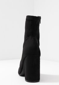 Schwarze Wildleder-Ankle-Boots mit runder Spitze, hohem, klobigem Absatz und Reißverschluss auf der Rückseite. Glatte Textur und nahtloses Design.