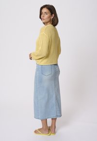 Jersey amarillo de punto con un corte relajado, combinado con una falda larga de mezclilla azul clara. El conjunto se completa con chanclas amarillas.