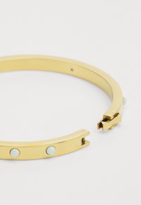 Gold-tone bracelet with a smooth, rounded design featuring three small, round opalescent stones. Includes a secure clasp mechanism.