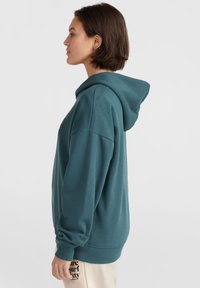Felpa con cappuccio color turchese, dal fit rilassato, con polsini e fondo a coste. Presenta una stampa minimalista sul davanti e dettagli laterali vicino all'orlo.