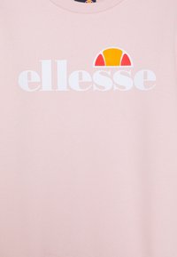 Sudadera rosa claro con cuello redondo. Presenta un logo blanco de "ellesse" y un gráfico colorido de un sol sobre el texto. Textura suave.