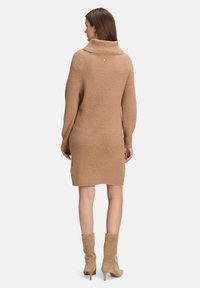 Beige Strickkleid mit hohem Kragen, gerippter Textur und langen Ärmeln. Hat eine kleine Verzierung auf der Rückseite.