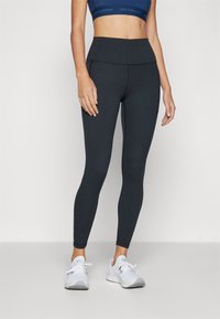 Leggings neri in un materiale elegante e elastico con vita alta. Abbinati a un reggiseno sportivo blu navy e scarpe da ginnastica bianche.