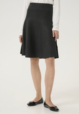 Una gonna svasata di colore grigio scuro, realizzata in tessuto texturizzato, con una vita liscia, abbinata a scarpe nere senza tacco con un dettaglio a fiocco.