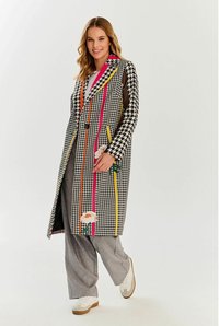Płaszcz w wzór houndstooth w czerni i bieli, z kolorowymi paskami i haftem kwiatowym. Długi, dopasowany fason z kołnierzem i zapięciem na guziki.