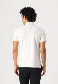 Polo shirt blanc en coton, avec un col et des manches courtes. Le dos présente un design minimaliste avec un subtil détail de couture.
