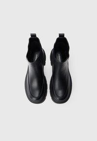 Bottines en cuir noir avec une finition lisse, des panneaux élastiques sur les côtés et une semelle en caoutchouc épaisse. Équipées de tirettes à l'arrière pour un enfilage facile.
