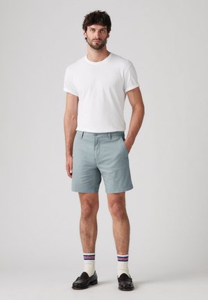 Light blue shorts made of a smooth fabric, featuring a classic fit and side pockets, paired with a plain white t-shirt and striped socks.