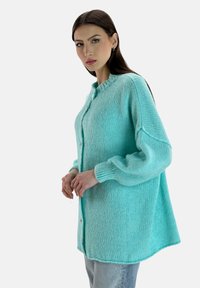 Türkiser Strickcardigan mit Rundhalsausschnitt, Knopfverschluss, fallenden Schultern und gerippten Bündchen. Weicher Stoff mit entspannter Silhouette.