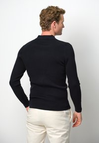 Schwarzer Strickpullover mit tailliertem Schnitt, langen Ärmeln und Kragen. Strukturierter Stoff mit gerippten Details an den Schultern und Manschetten.