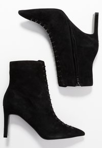 Bottines en daim noir avec bout pointu, fermeture éclair latérale et laçage décoratif sur le devant. Talon aiguilles élevé.