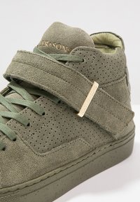 Zapatillas de ante verde oliva con un acabado texturizado, paneles perforados, una amplia correa de Velcro y un detalle en dorado.