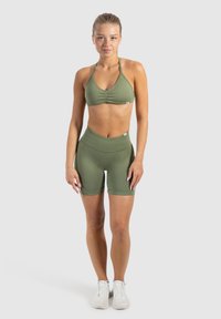Olivegroene sportbeha met plooien, gecombineerd met high-waisted bijpassende shorts. Zachte textuur, nauwsluitend ontwerp en minimale merkdetail.