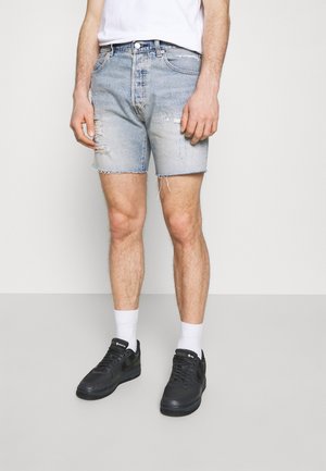 Shorts en denim délavé avec des détails usés, ourlet effiloché et coupe décontractée. Associés à des baskets noires et des chaussettes blanches mi-mollet.