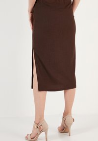 Fustă midi ribbed de culoare maro, cu o fanta laterală, din material texturat și o siluetă ajustată, asortată cu sandale cu toc bej.