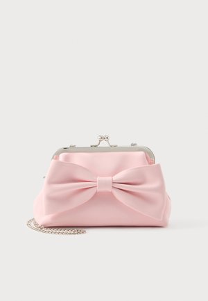 Cartera de mano rosa pálido con un gran lazo en la parte delantera, cierre plateado y correa de cadena plateada, sobre una superficie lisa y clara.