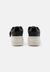 Czarne lakierowane sneakersy na białej platformie. Posiadają teksturowane zapięcie, logo oraz srebrne detale po boku.