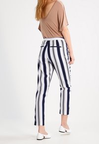 Hnědý top s krátkým rukávem, námořnické a bílé pruhované úzké kalhoty s vysokým pasem a dvěma zadními kapsami. Bílé ploché boty.