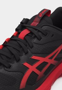 Αθλητικό παπούτσι σε μαύρο και κόκκινο με υφασμάτινη υφή, μαύρα κορδόνια, κόκκινες λεπτομέρειες και το λογότυπο της ASICS στο πλάι και στη γλώσσα.