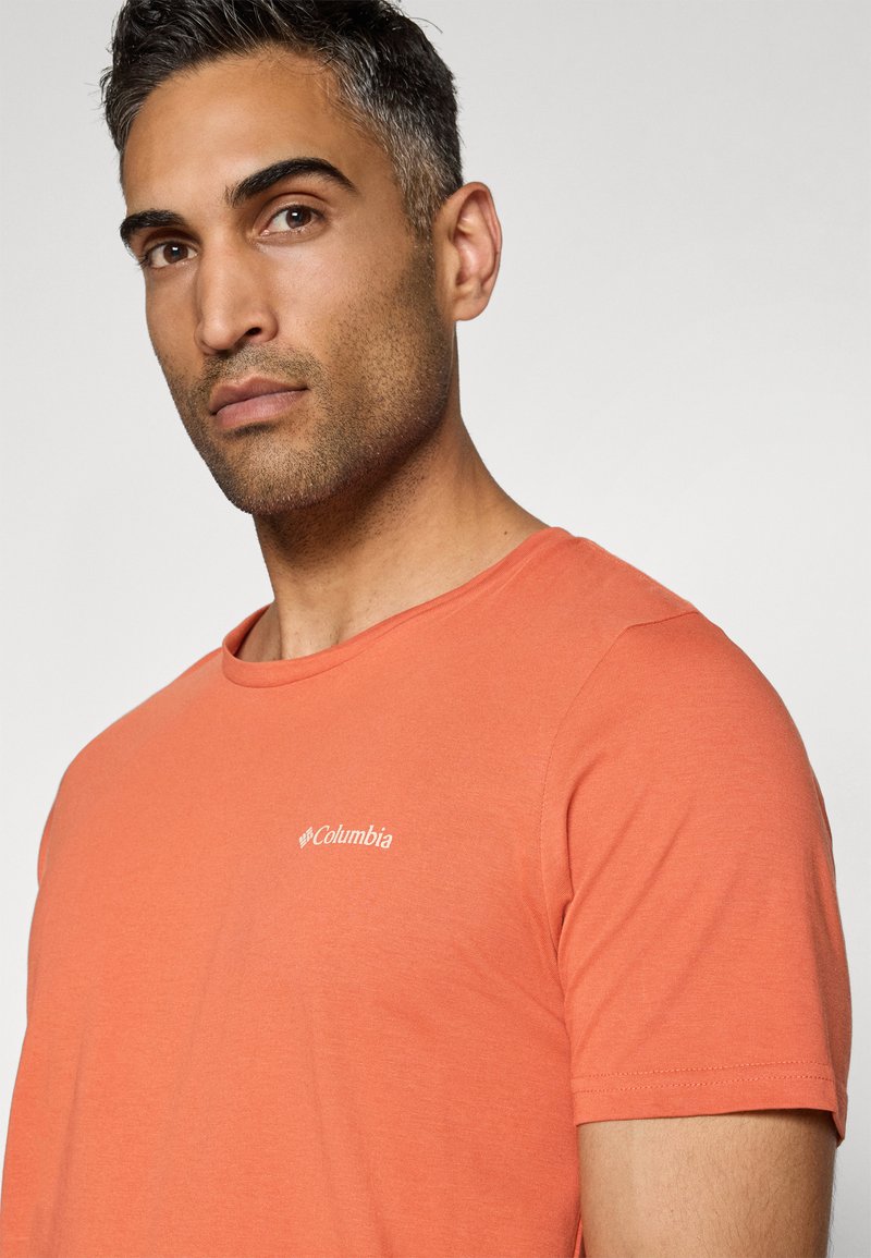 Kurzärmeliges oranges T-Shirt aus weichem Stoff, mit einem Rundhalsausschnitt und einem kleinen weißen Columbia-Logo auf der linken Brust.