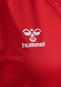 Roter Stoff mit einem weißen "hummel"-Logo, gestaltet mit einer stilisierten Bienen-Grafik und abstrakten Formen, glatte Textur.