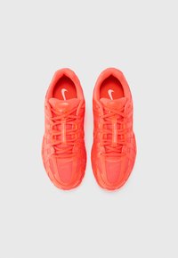Ryškiai koralų spalvos Nike sportiniai bateliai, pagaminti iš tinklinės ir sintetinės medžiagos, su storu padu, ryškiais raišteliais ir logotipu ant liežuvėlio.