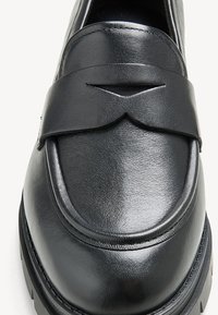 Mocassin en cuir noir avec une texture lisse, un bout rond et une bande décorative avec un détail découpé à l'avant.
