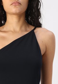 Black, sleeveless top with a diagonal neckline. Made of smooth, lightweight fabric. Features thin shoulder strap and subtle curve at bust.