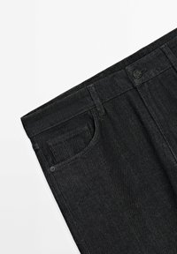 Gros plan sur la taille d'un jean en denim noir avec un bouton, des passants de ceinture, une poche avant et une poche monnaie sur fond blanc.
