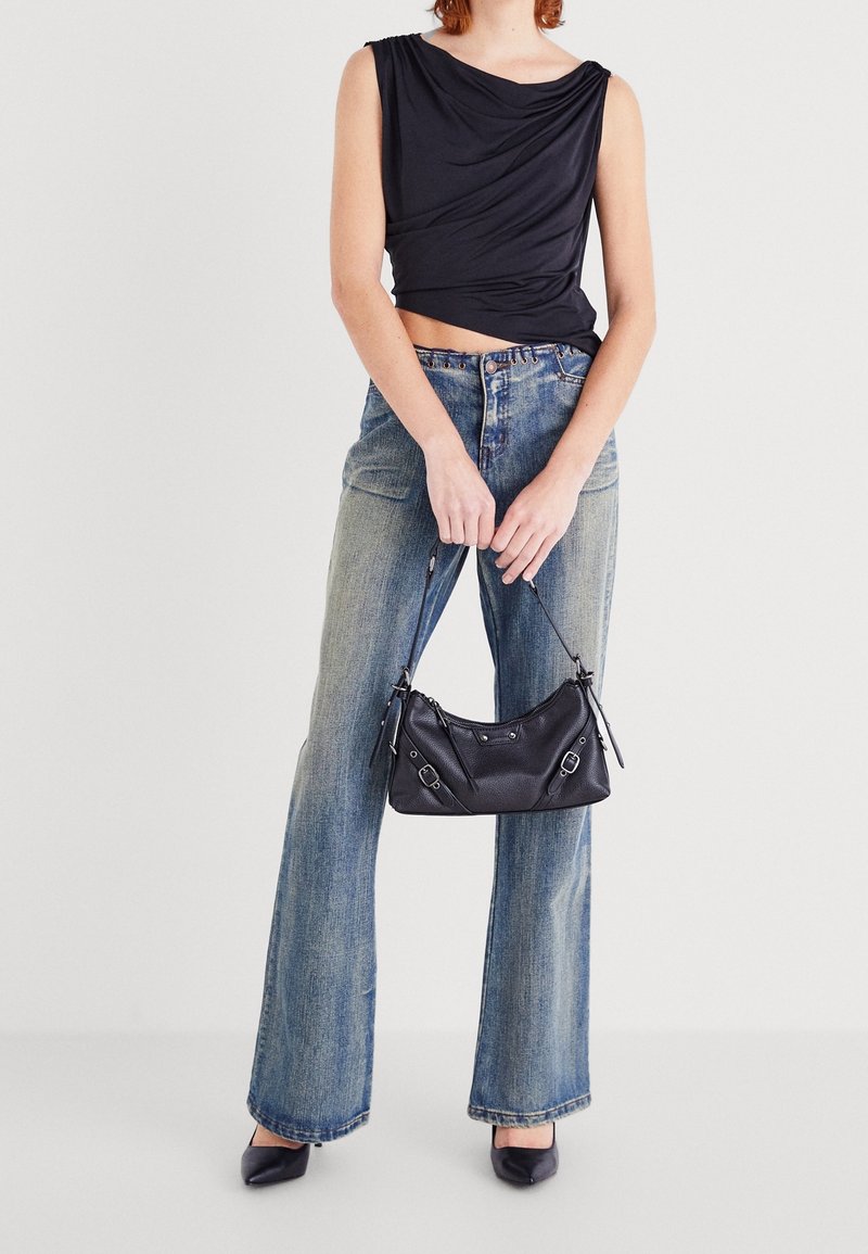 Top noir sans manches avec un design drapé, jean bleu taille haute, sac à main noir avec rabat, et escarpins noirs à bout pointu.