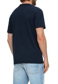 Marineblauwe katoenen t-shirt met korte mouwen, ronde hals, en een ontspannen pasvorm. G gedragen met lichtblauwe jeans, met een eenvoudig ontwerp en een zachte textuur.