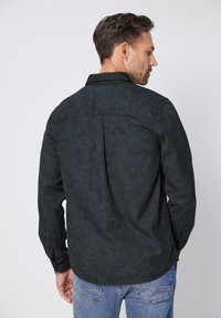 Czarna koszula w wzory z długimi rękawami i kołnierzykiem zapinanym na guziki. Posiada teksturowany wzór oraz ozdobny tylny karczek. Połączona z niebieskimi dżinsami.