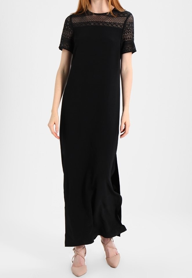 Robe maxi noire avec des manches courtes en dentelle et un buste uni. Présente une coupe décontractée et des fentes latérales pour faciliter les mouvements. Texture douce.