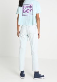 Svetle modré zkrácené tričko s fialovým textovým grafikou na zádech, spárované se svetle modrými džíny a tmavě modrými vysokými teniskami.