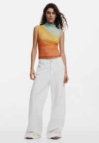 Ärmelloses Top mit orange-blauem Verlauf und drapiertem Stoff; kombiniert mit weißen, weit geschnittenen Hosen. Flache Schuhe sind am unteren Rand sichtbar.
