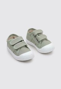 Une paire de chaussures pour tout-petits vert clair avec des semelles en caoutchouc blanches et deux bandes Velcro sur un fond gris neutre.