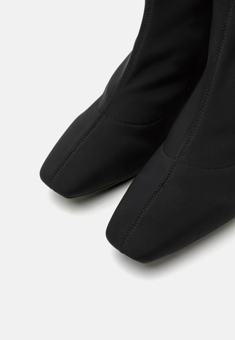 Czarne botki sięgające kostki, wykonane z teksturowanej tkaniny, z wąskim noskiem i subtelnymi przeszyciami wzdłuż boków.