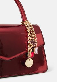 Rød lakk lærveske med en strukturert design, som har en gullkjedeaccent, dekorative charms og en logo-tag.