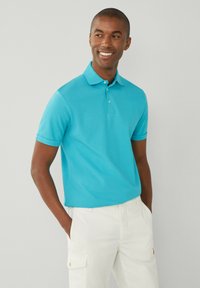 Kortärmad turkos polo skjorta i slät tyg, med krage och tre-knapps knäppning, som bärs tillsammans med ljusa cargoshorts.