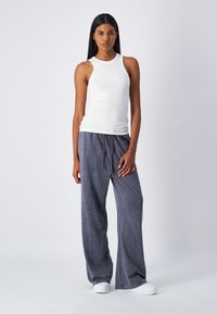 Canottiera bianca senza maniche abbinata a pantaloni della tuta grigi scuri e larghi con coulisse. I pantaloni presentano una consistenza morbida e un delicato effetto lavato.