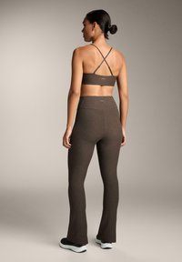 Barna sportmelltartó keresztpántokkal, barna harangszárú leggings-szel párosítva. Az öltözet sima textúrájú és testhezálló kialakítású.