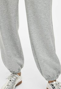 Graue Sweatpants aus weichem Material mit elastischem Bund und Bündchen. Kombiniert mit reflektierenden silbernen Sneakers.