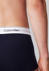 Boxeri scurți Calvin Klein de culoare bleumarin, cu un elastic alb inscripționat cu text negru, design ajustat și țesătură netedă, elastică.